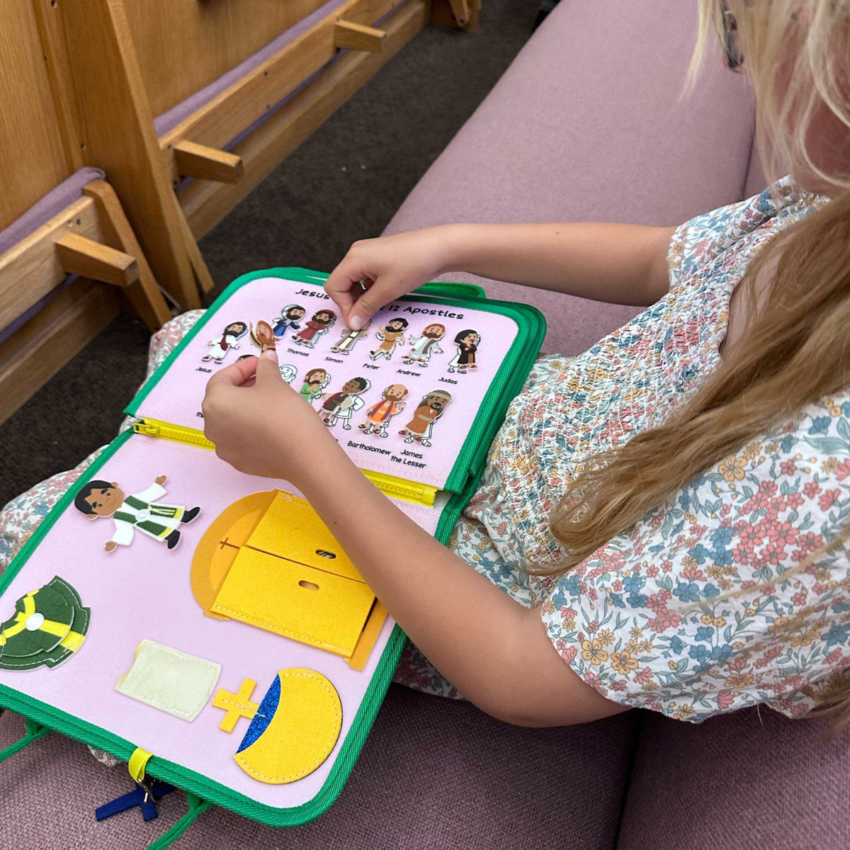 Child holding open green-edged felt busy book with puzzle pieces and cards