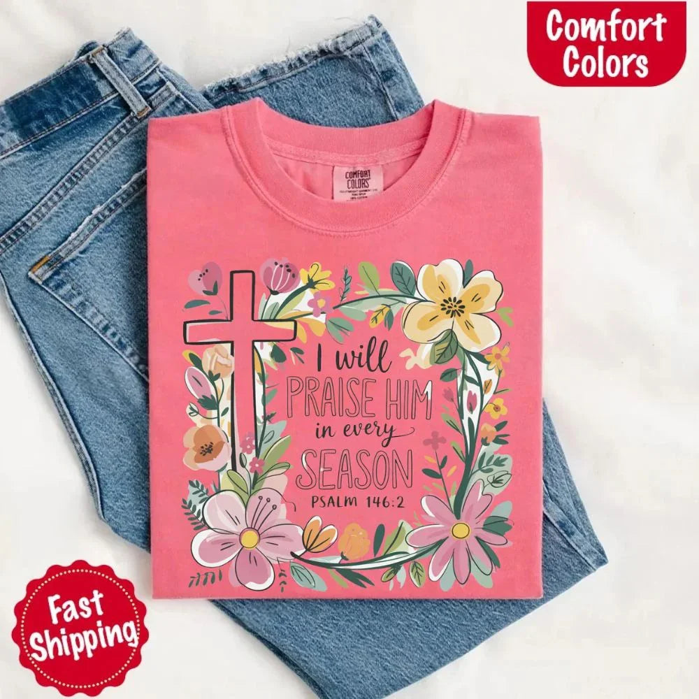 Pink comfort tee front with floral cross and “I will praise him in every season” lettering