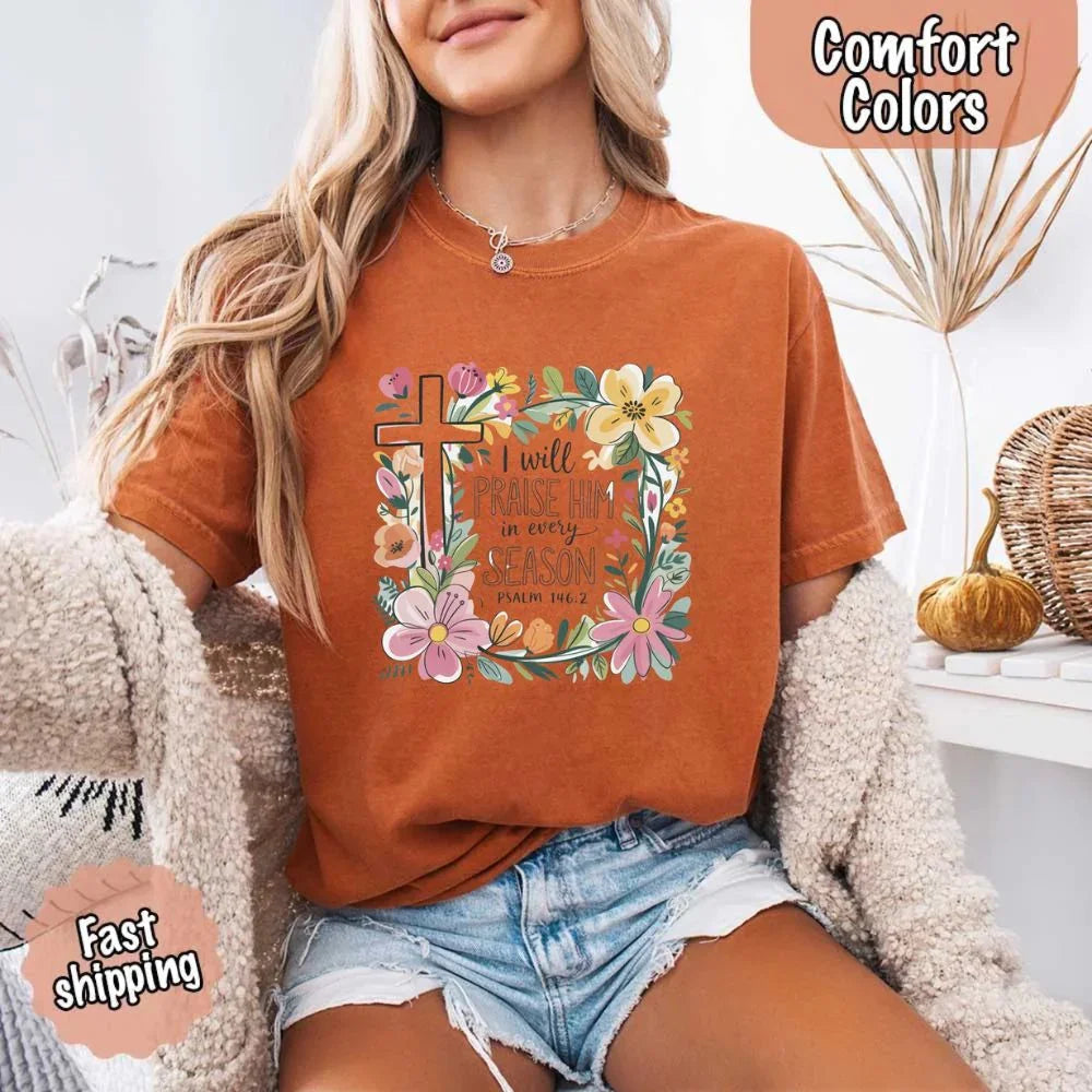 Rust orange comfort tee with floral cross and “I will praise him in every season” graphic