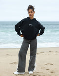 Black unisex hoodie with hood and small chest graphic, worn with jeans