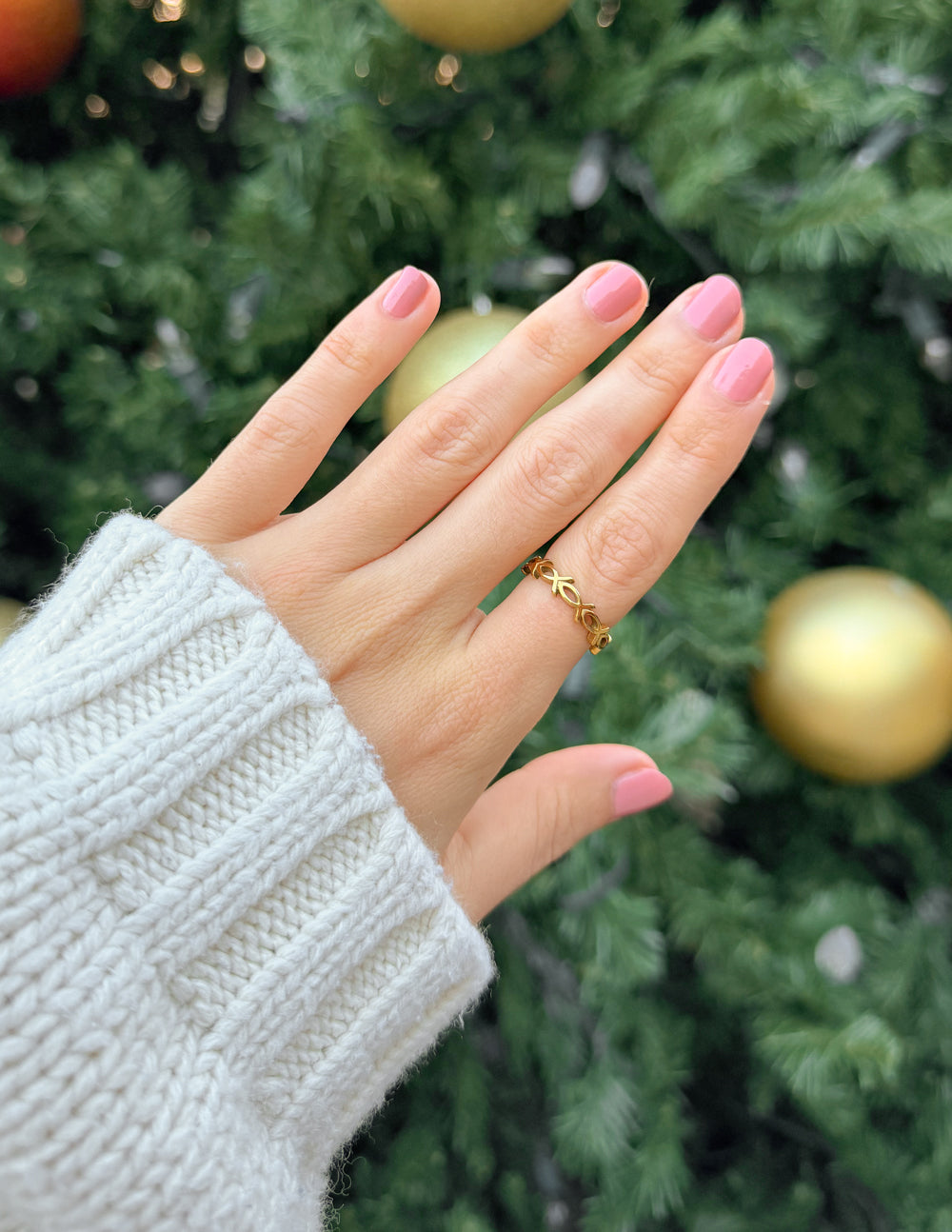 Gold infinity fish ring on hand, finger-worn band with linked fish design.