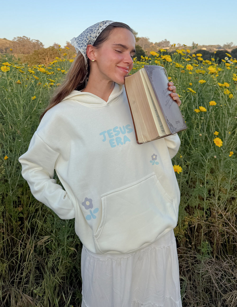 Cream unisex hoodie with “JESUS ERA” chest print and small blue flower accents
