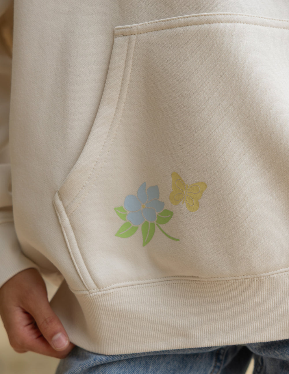 Unisex hoodie, cream, sleeve seam and small floral graphic near pocket