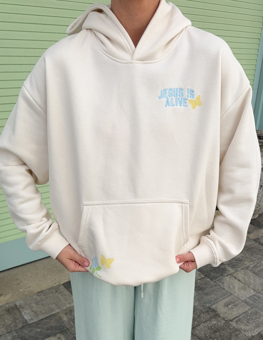 Unisex hoodie, cream, front chest graphic “JESUS IS ALIVE” above kangaroo pocket