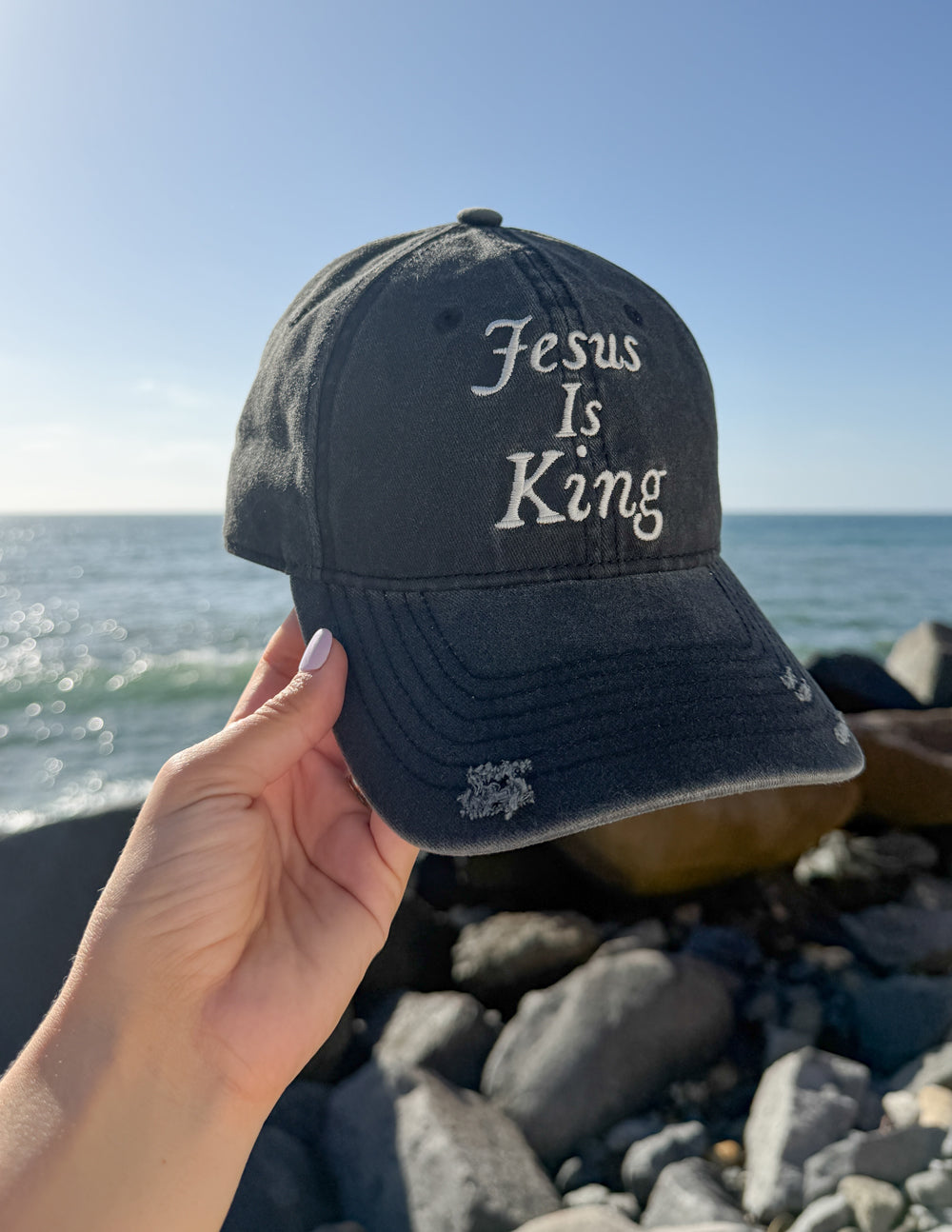 Black baseball cap held in hand, front says “Jesus Is King”