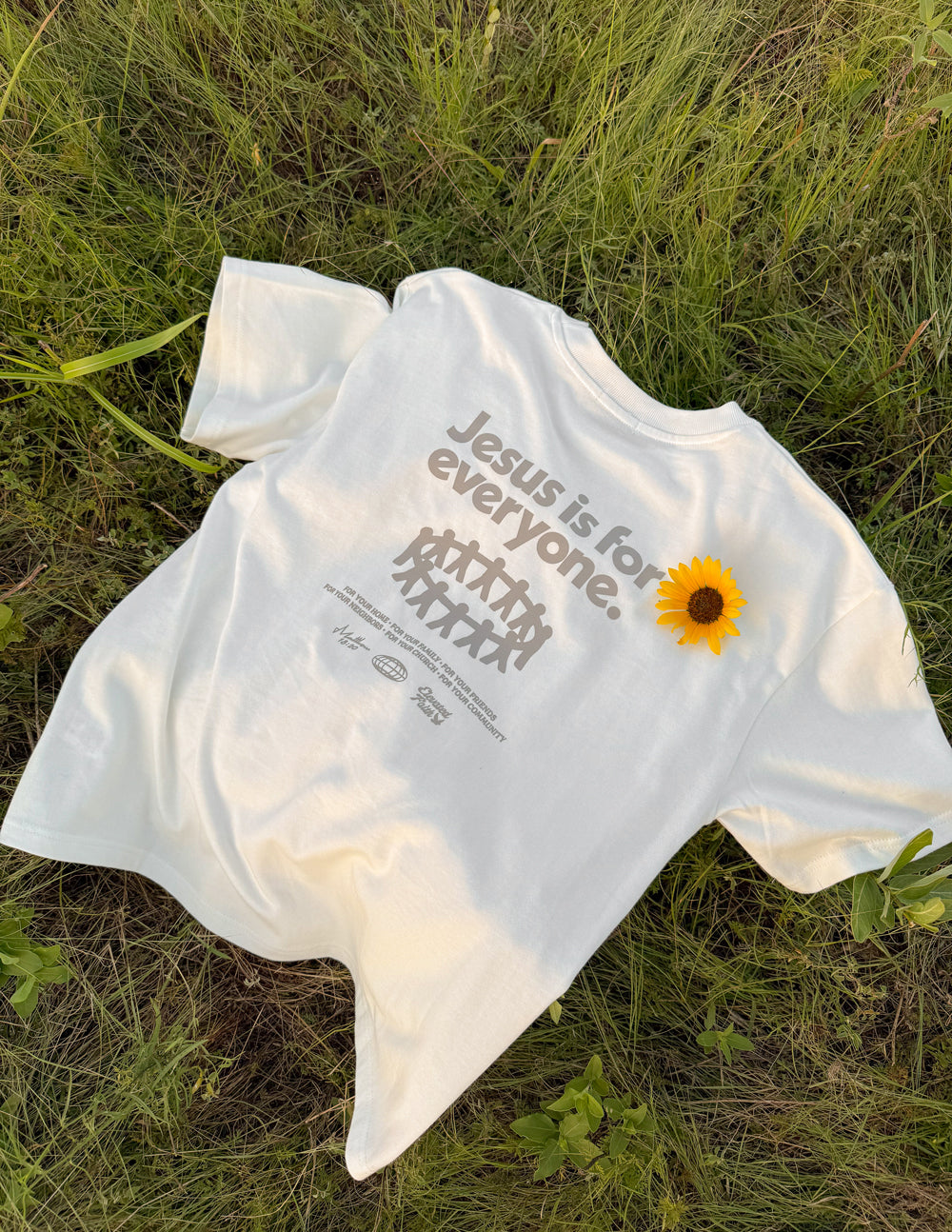 White heavyweight graphic T-shirt laid on grass with front print and yellow flower graphic