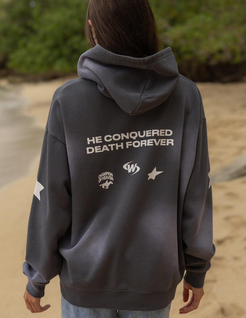 Dark gray unisex hoodie with hood and front pocket, back print “THE CONQUERED DEATH FOREVER”