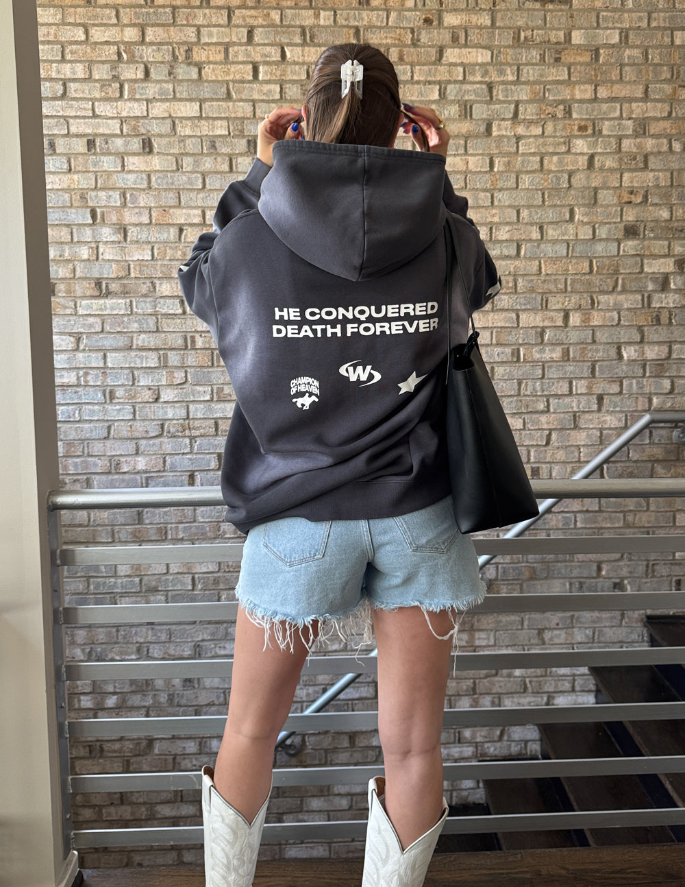 Dark gray unisex hoodie with hood and front pocket, back text “THE CONQUERED DEATH FOREVER”