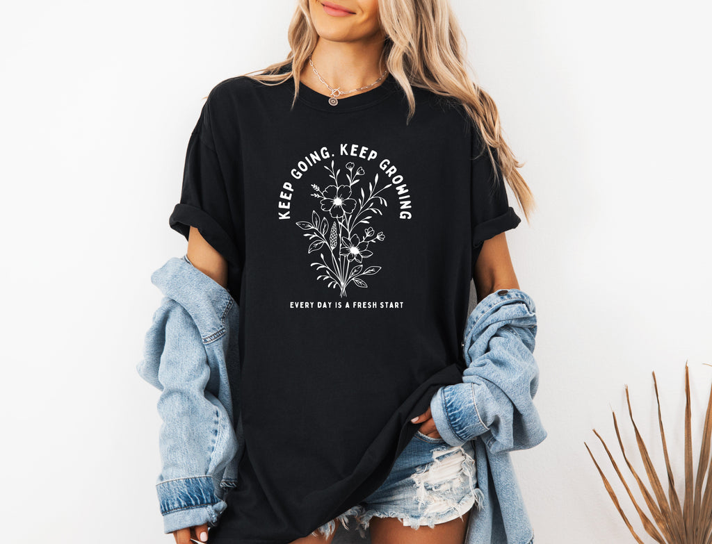 Black unisex T-shirt with white botanical floral quote graphic on front.