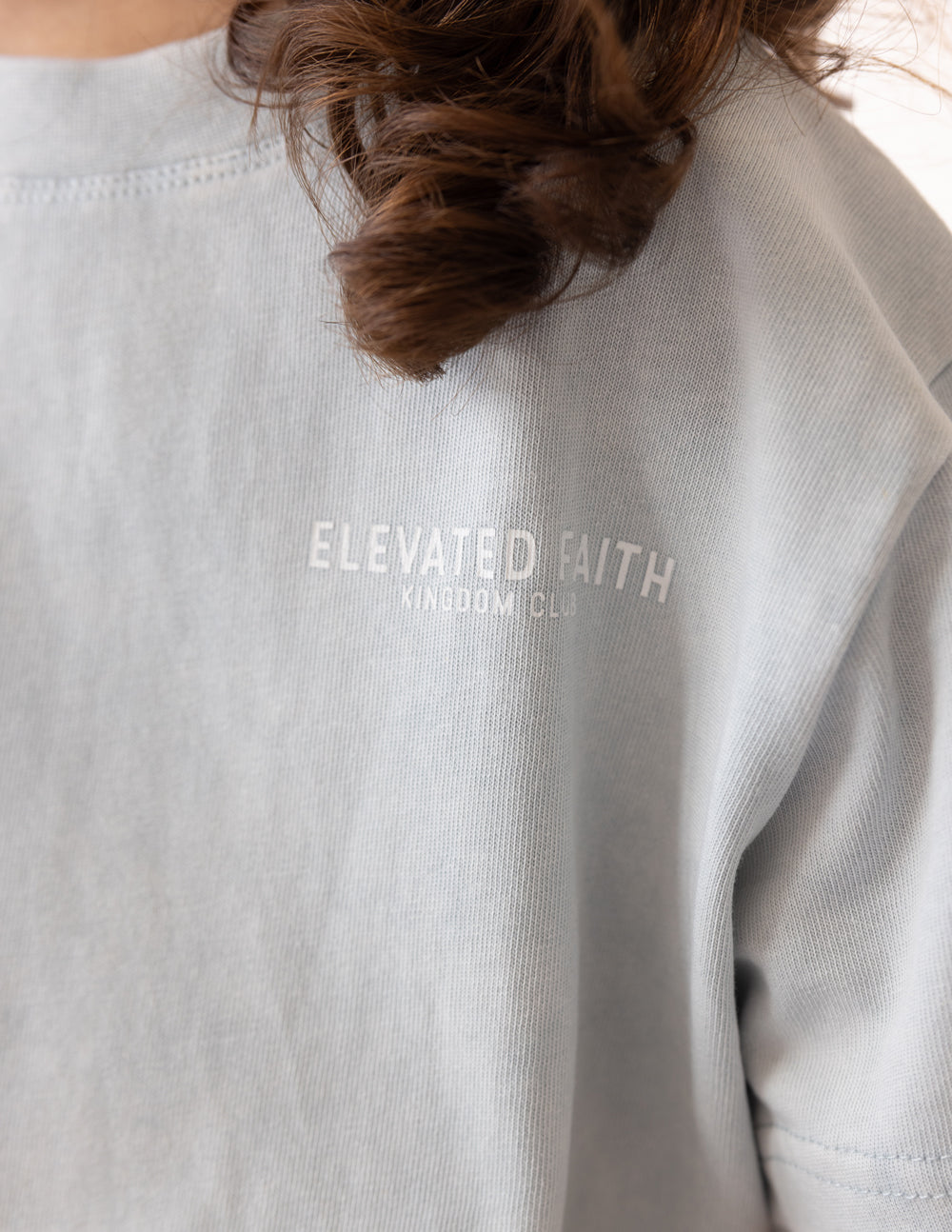 Kids light gray crewneck tee, close-up of "ELEVATED FAITH" back print