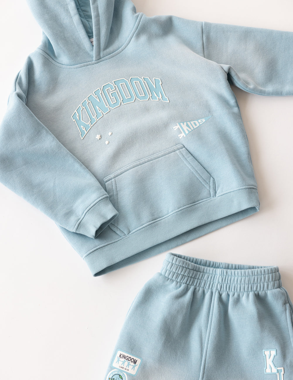 Kids light blue hoodie flat lay with Kingdom logo, hood, and kangaroo pocket