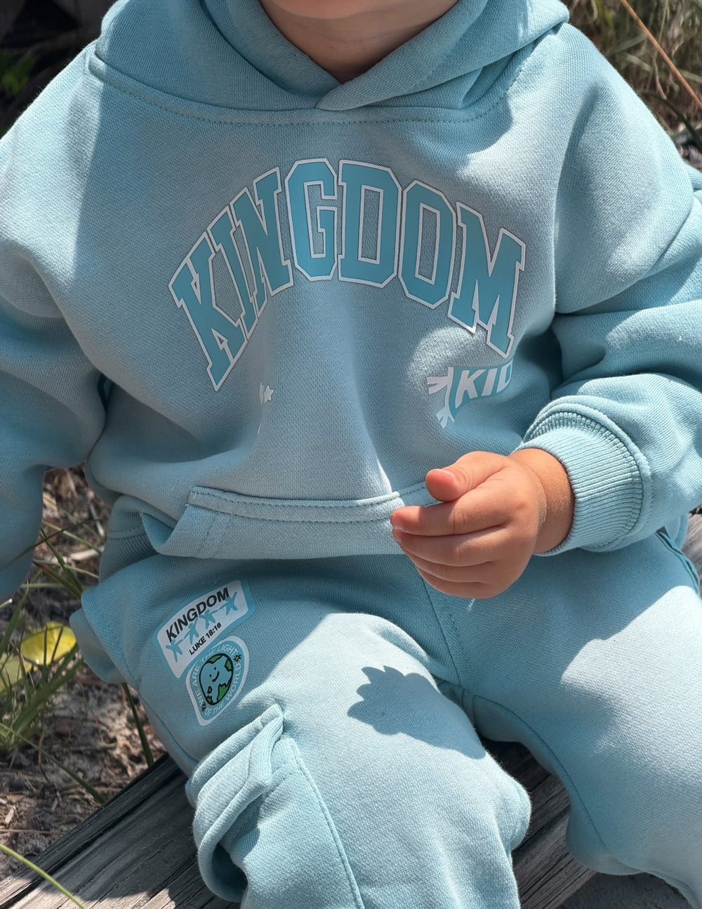 Kids light blue hoodie close-up with Kingdom logo and kangaroo pocket