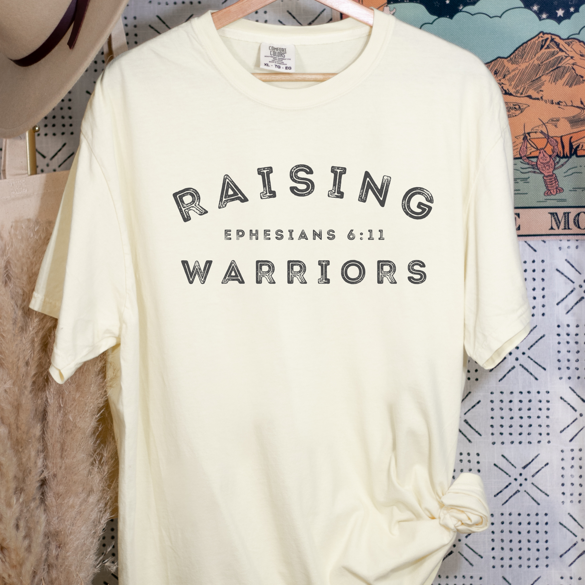Cream t-shirt with Raising Warriors Ephesians 6:11 front graphic