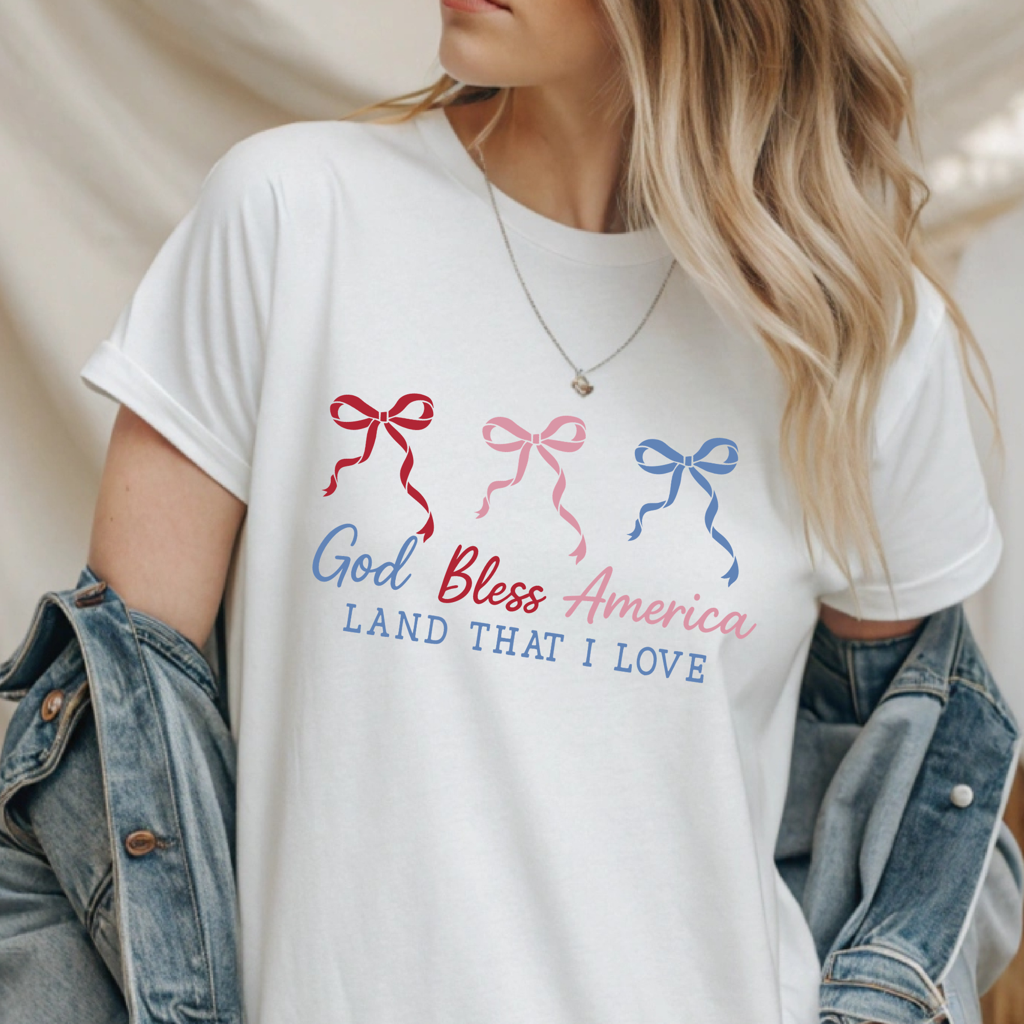 White crewneck T-shirt with bow graphic and “God Bless America” text in blue/red