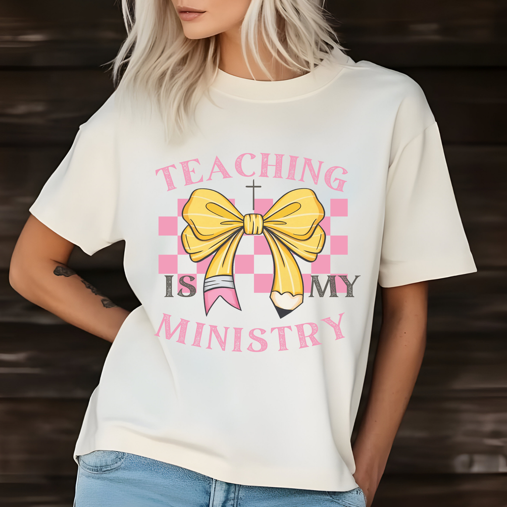 White short-sleeve T-shirt with pink 'TEACHING IS MY MINISTRY' text and yellow bow