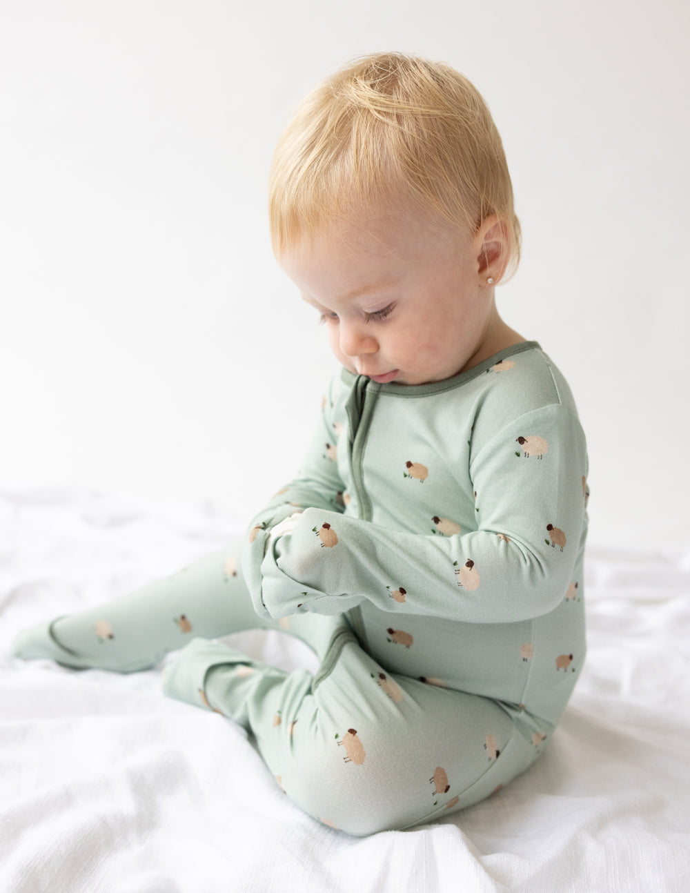 Sage green lamb-print baby onesie with front zip and footed legs