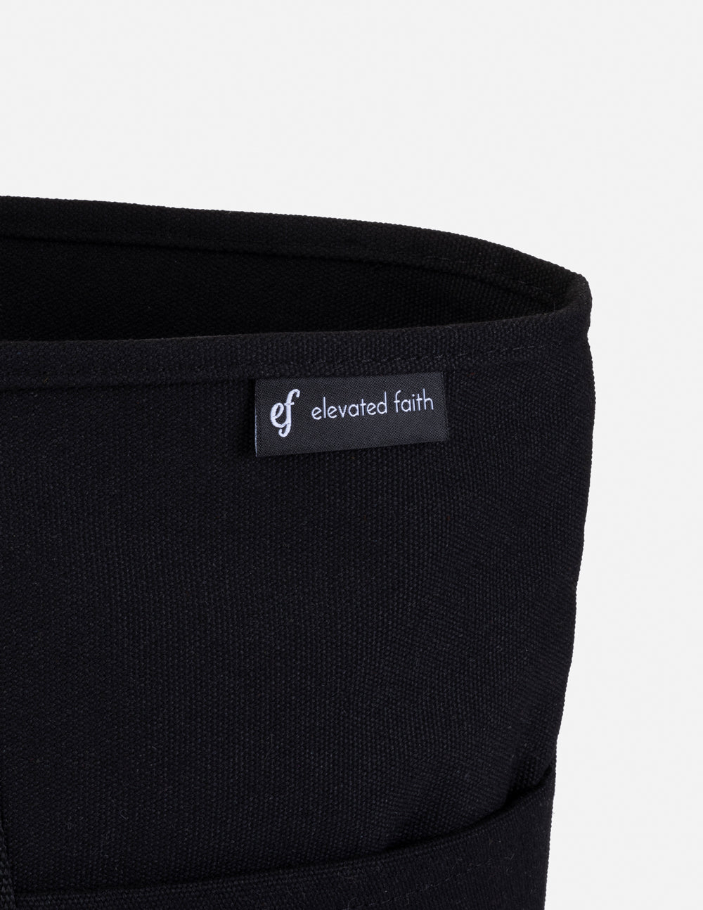 Black tote bag fabric close-up with “elevated faith” brand label inside pocket