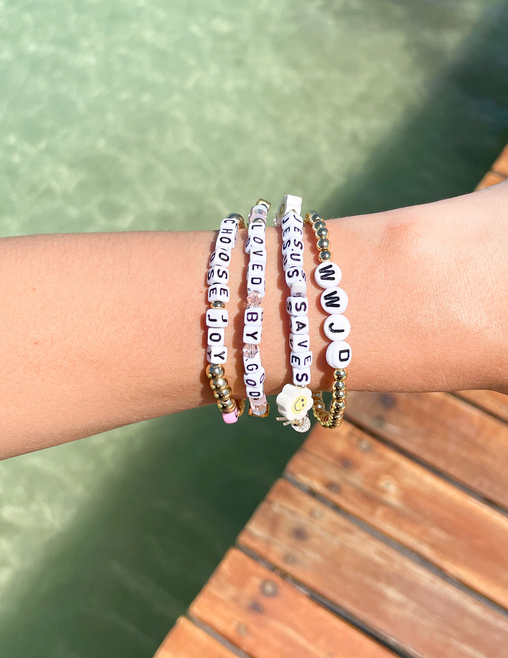 Beaded letter bracelets on wrist with purple and pink letter beads and gold-tone beads.
