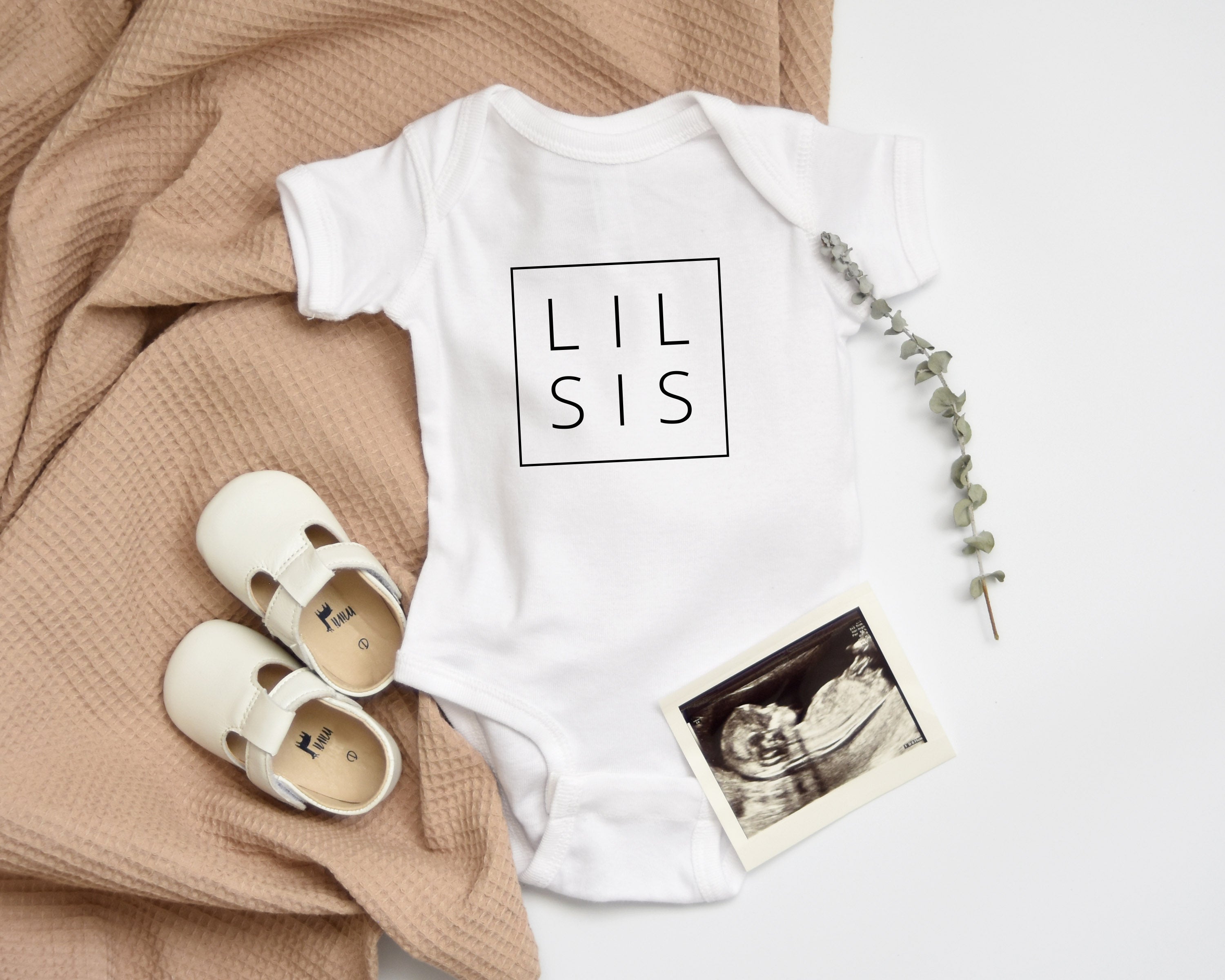 White baby bodysuit with LIL SIS logo print and snaps