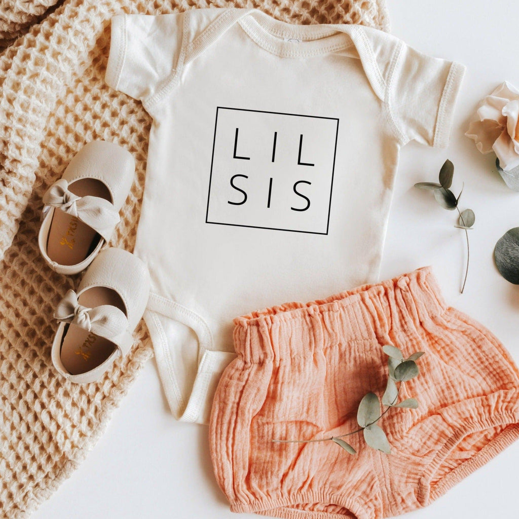 White baby bodysuit with square print reading LIL SIS