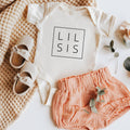 White baby bodysuit with square print reading LIL SIS