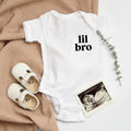 White baby onesie with short sleeves and "lil bro" printed front, snap closure at leg