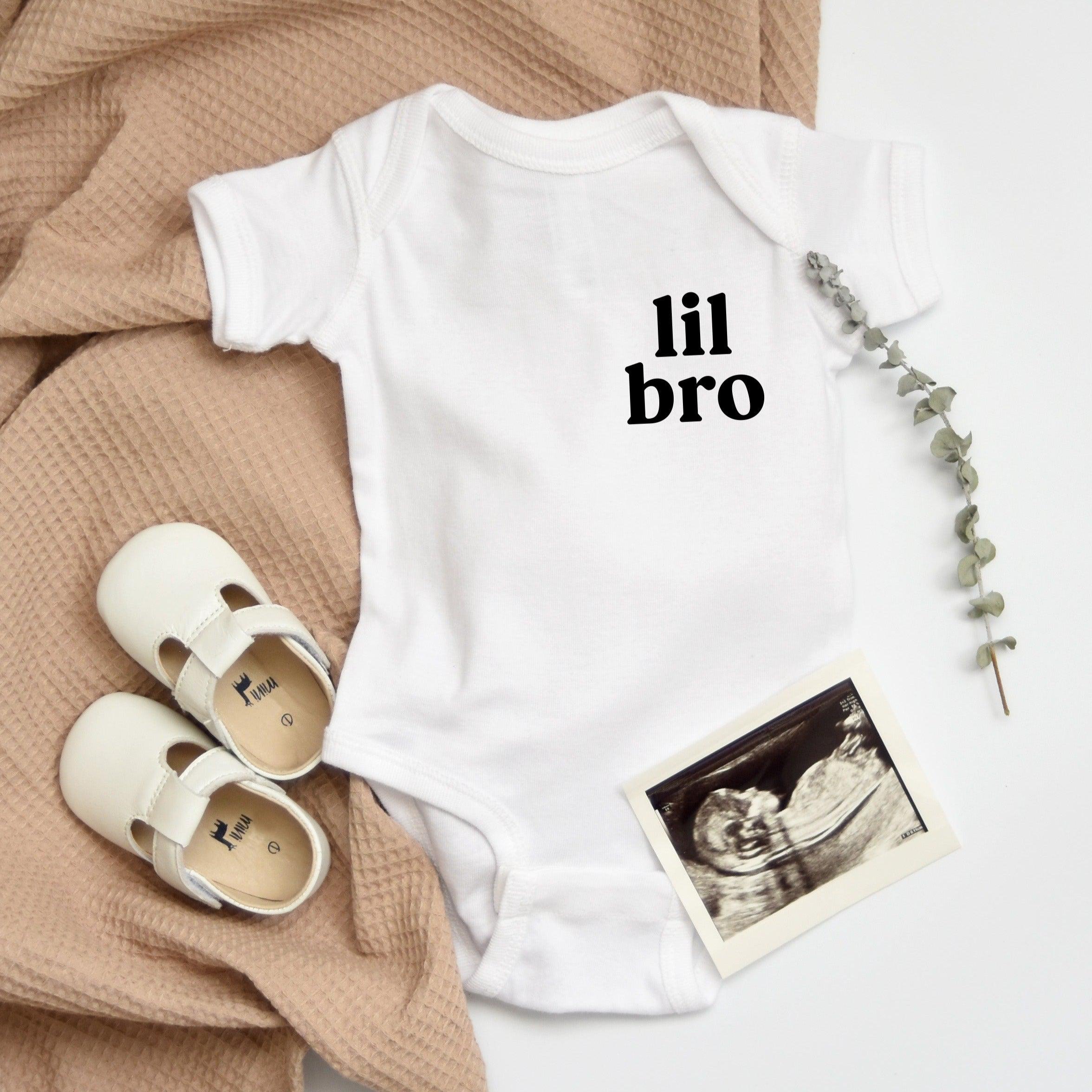 White baby onesie with short sleeves and "lil bro" printed front, snap closure at leg