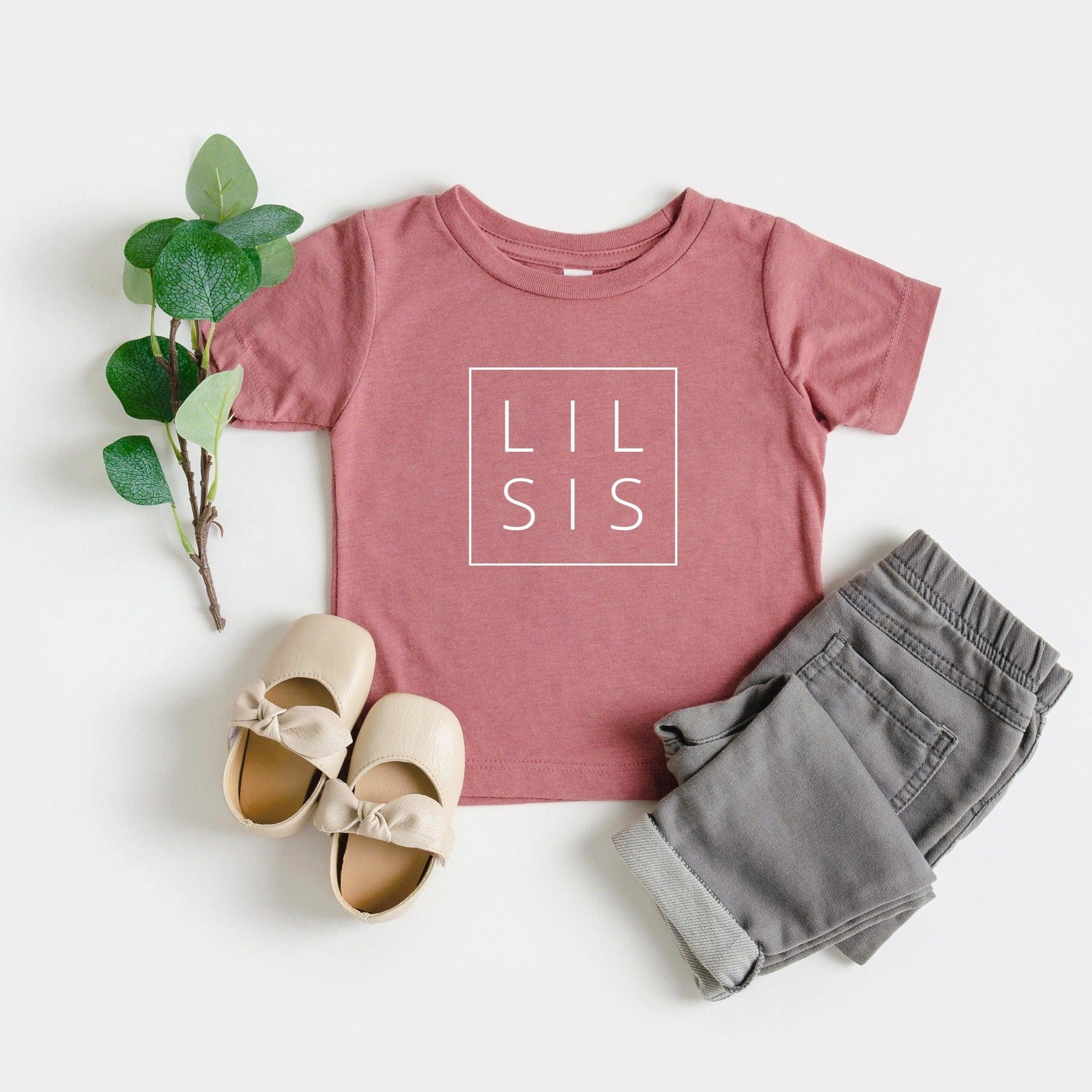 Pink baby toddler T-shirt with 'LIL SIS' logo in square frame