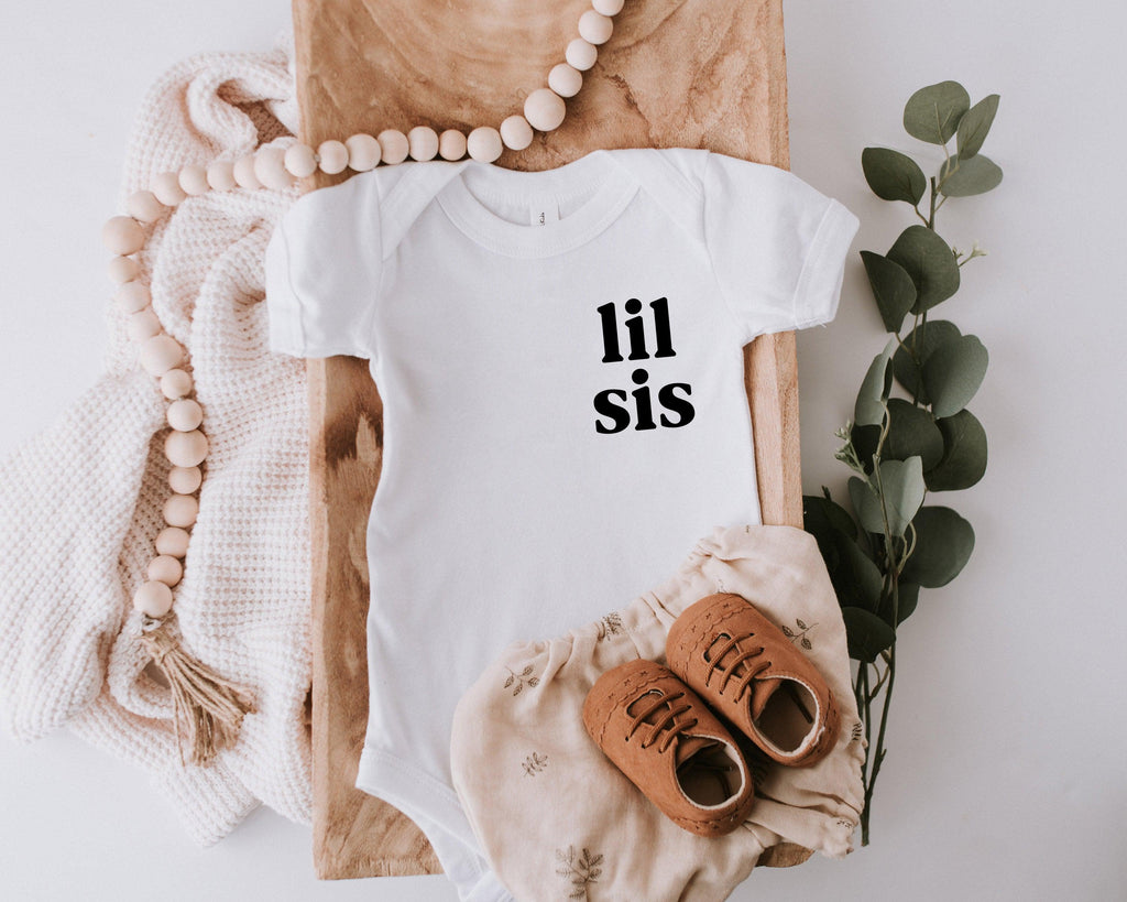 White baby onesie with 'lil sis' chest print, short sleeves and snap legs
