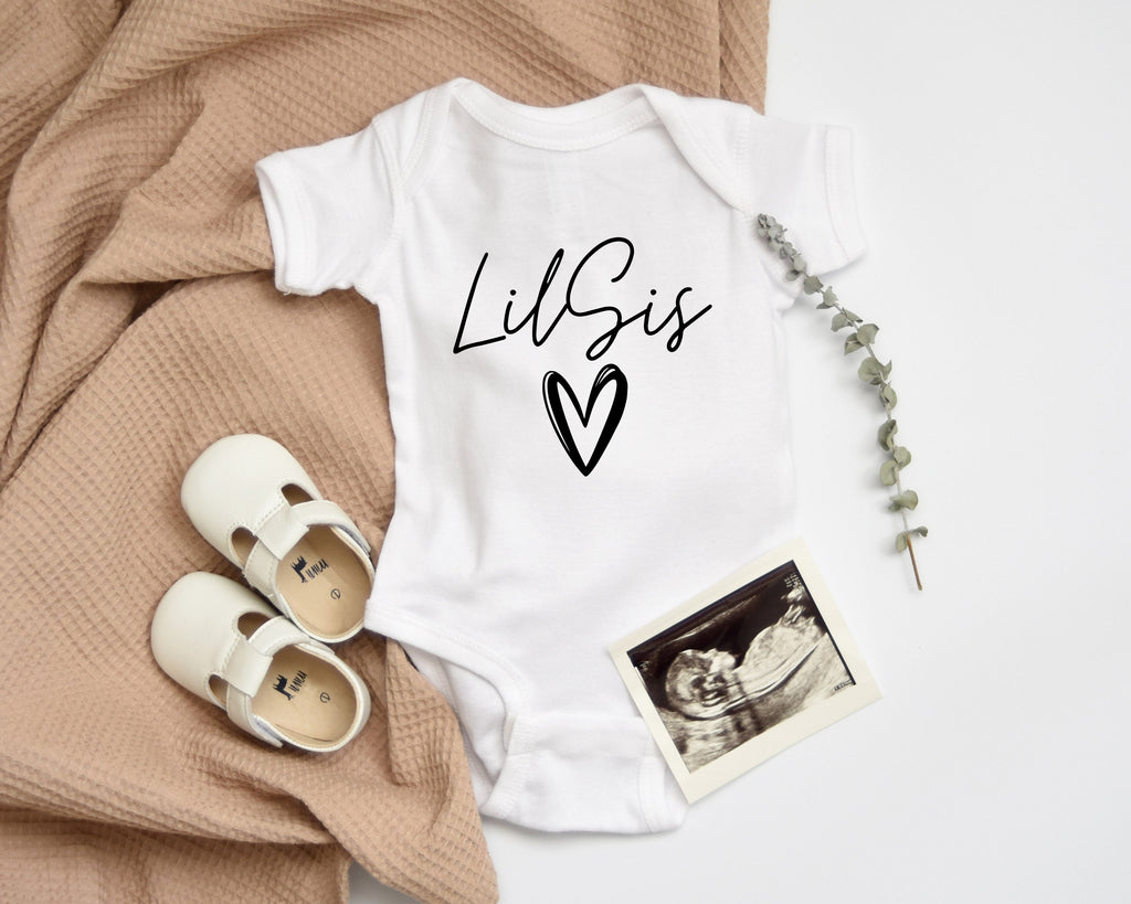 White baby onesie with black LilSIS cursive and heart icon, long sleeves