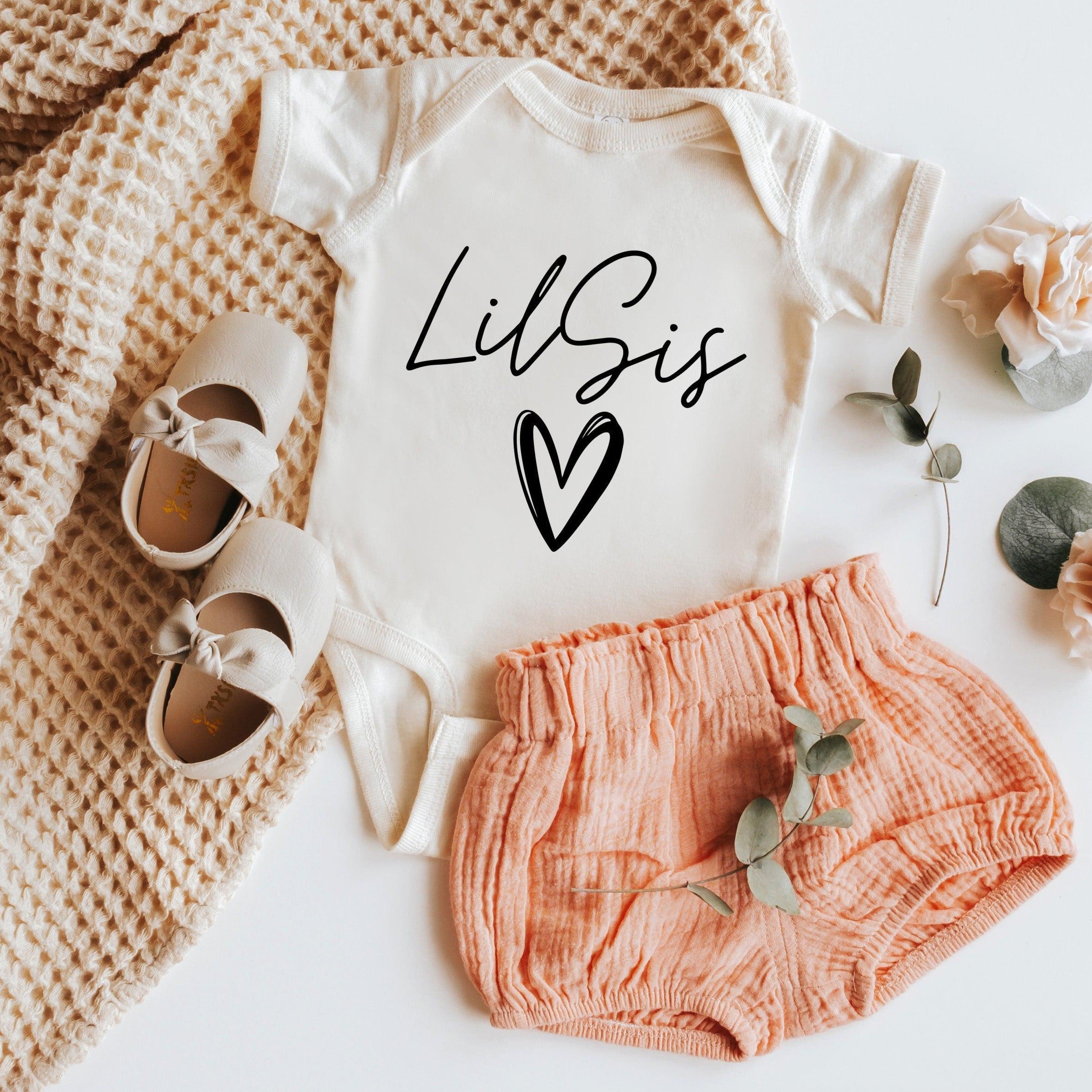 White baby onesie with black cursive LilSIS logo and heart, short sleeves