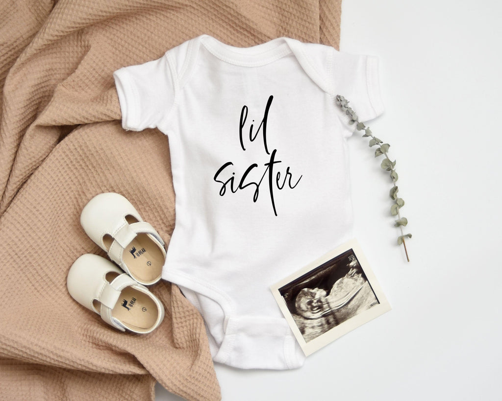 White baby bodysuit with black cursive "lil sister" print