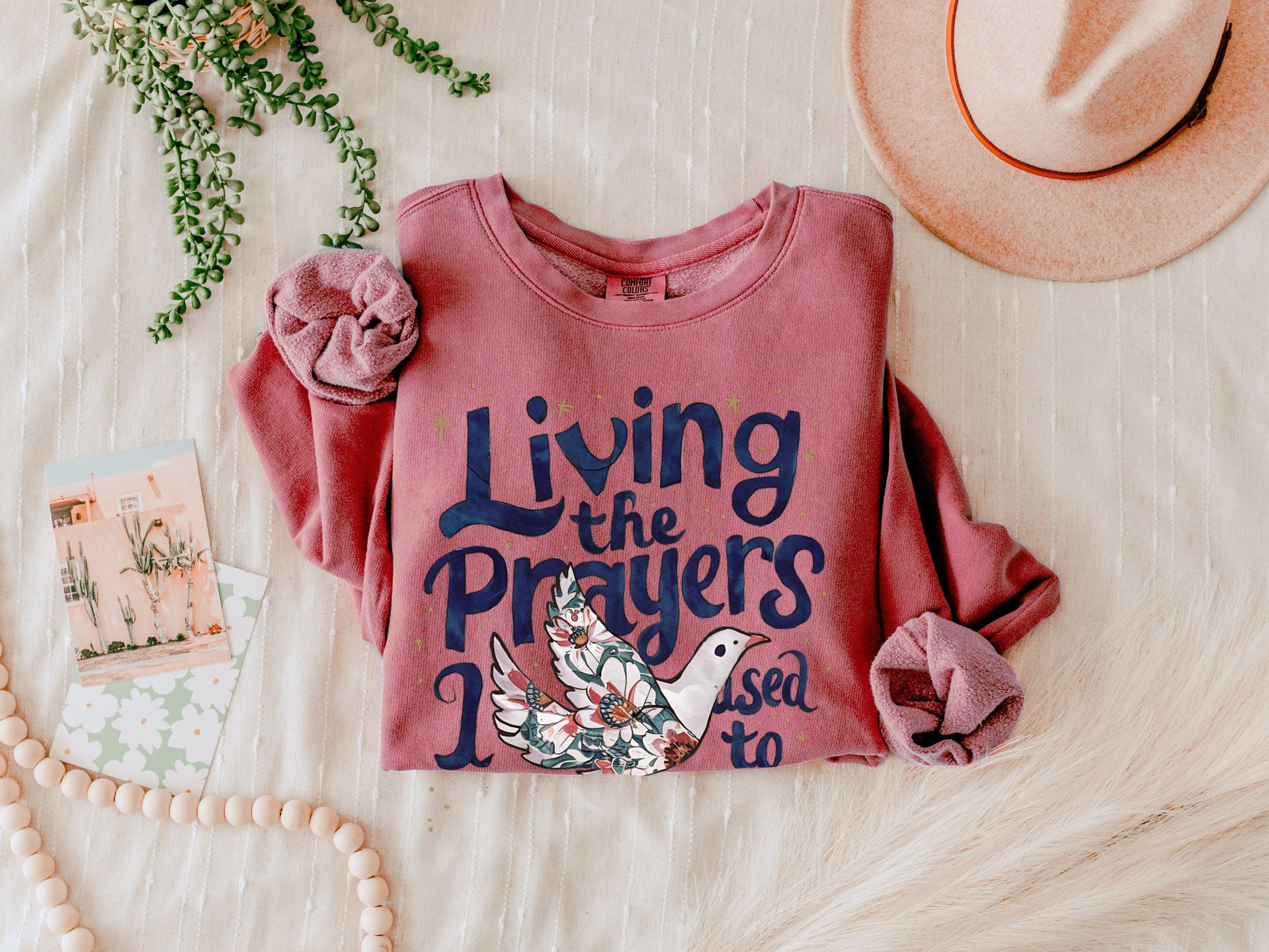 Dusty rose crewneck sweatshirt with "Living the Prayers" floral cross graphic