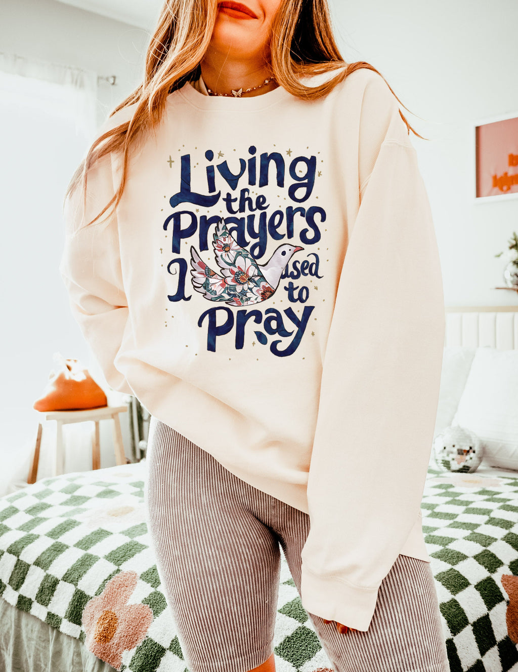 Cream crewneck sweatshirt with "Living the Prayers" floral cross graphic