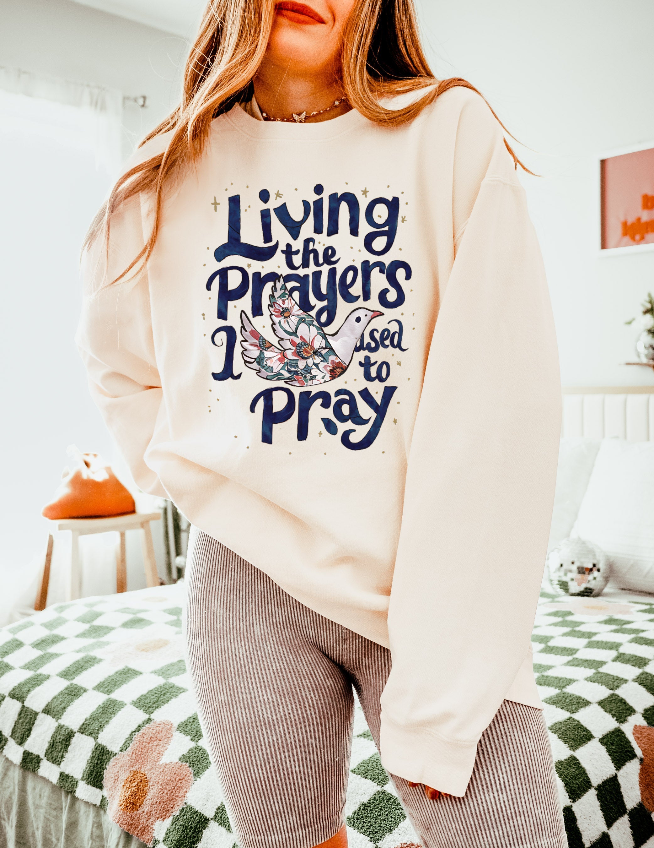 Cream crewneck sweatshirt with "Living the Prayers" floral cross graphic