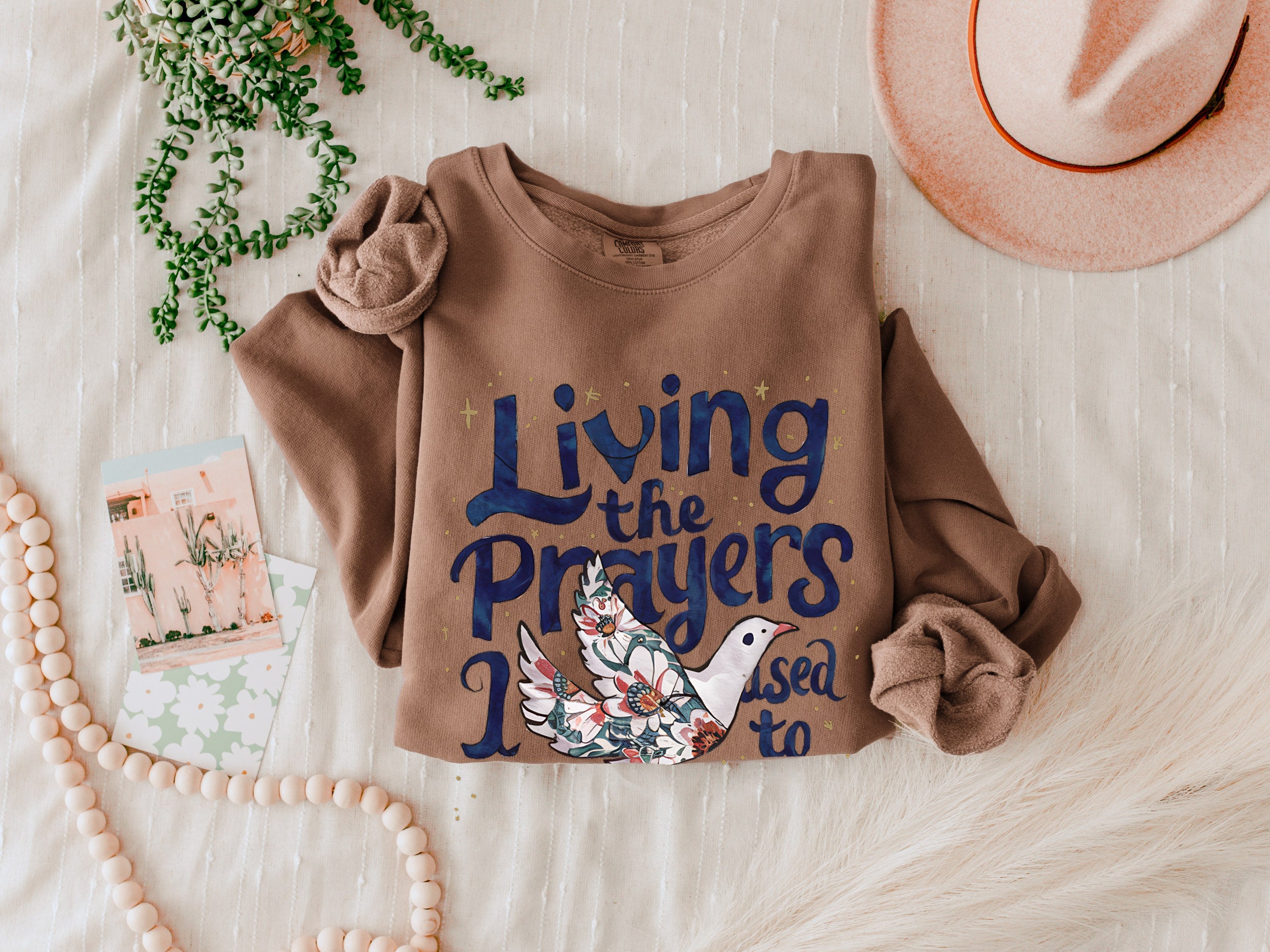 Brown crewneck sweatshirt with "Living the Prayers" floral cross graphic