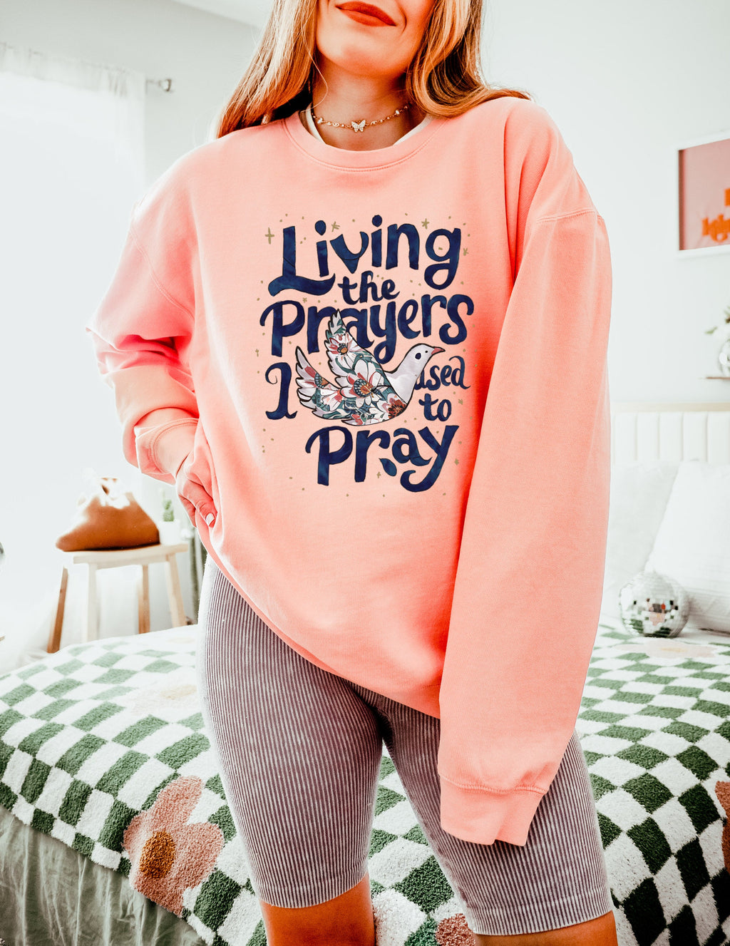Peach pink crewneck sweatshirt with "Living the Prayers" floral cross graphic
