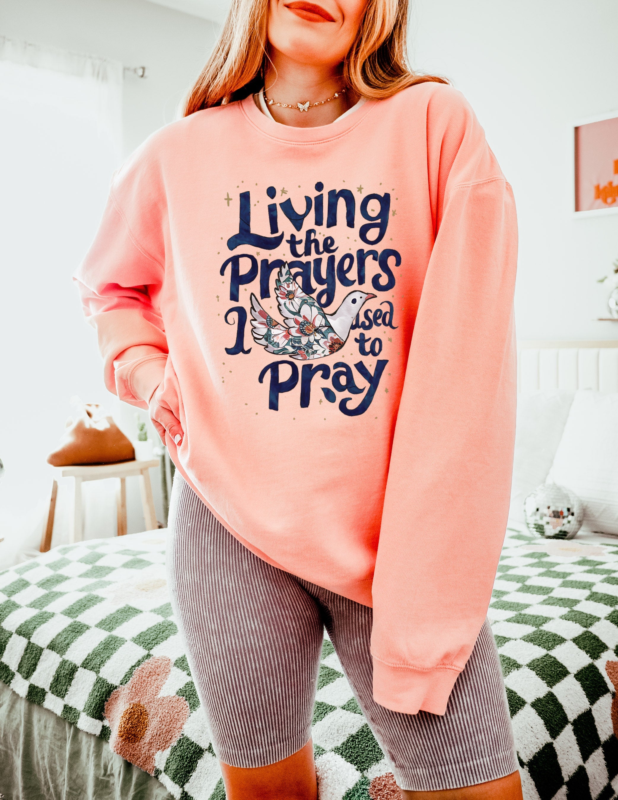 Peach pink crewneck sweatshirt with "Living the Prayers" floral cross graphic