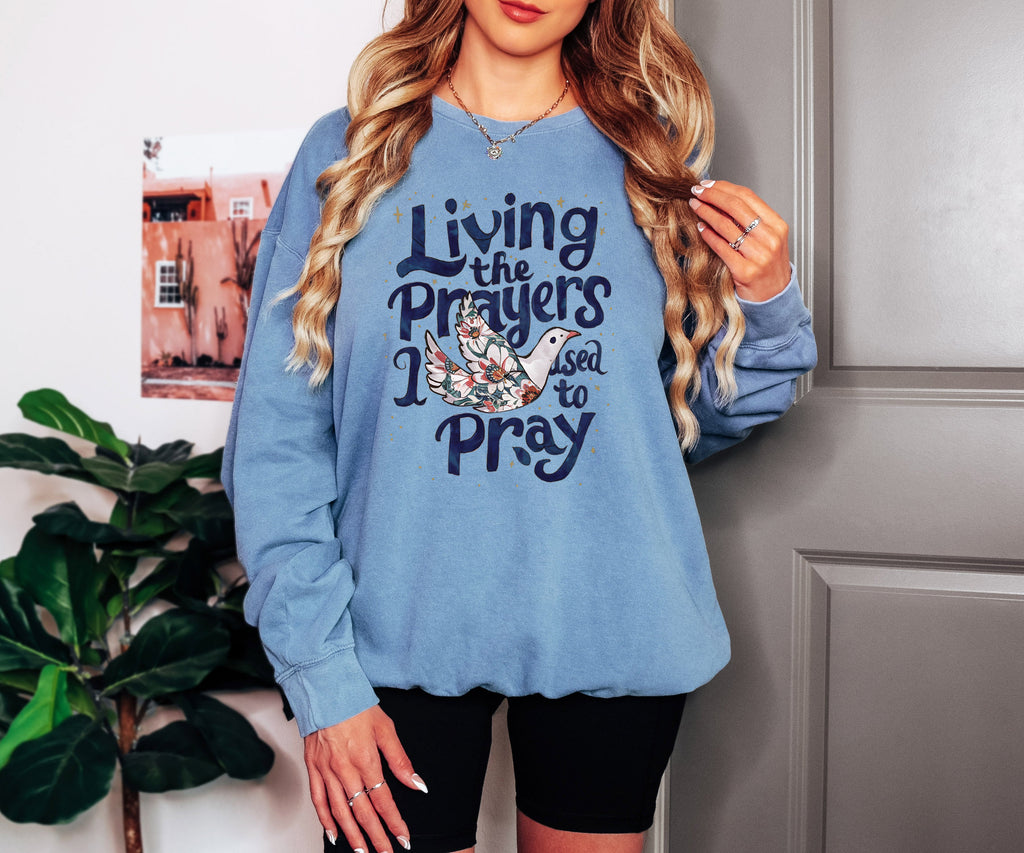 Medium blue crewneck sweatshirt with "Living the Prayers" floral cross graphic