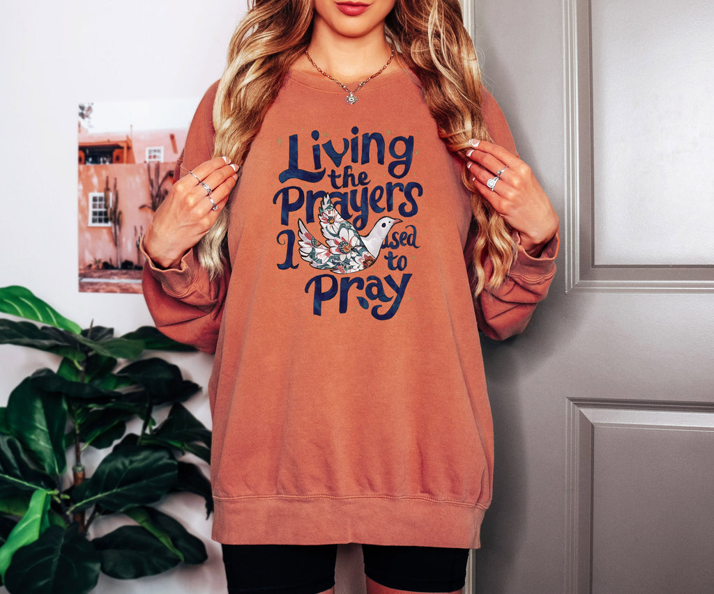 Rust orange crewneck sweatshirt with "Living the Prayers" floral cross graphic