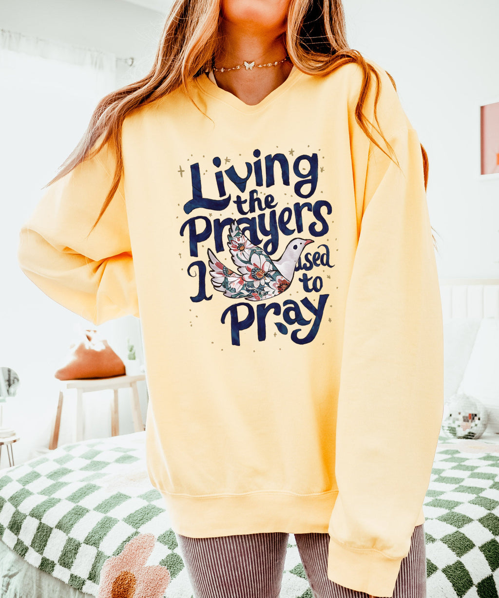 Yellow crewneck sweatshirt with "Living the Prayers" floral cross graphic
