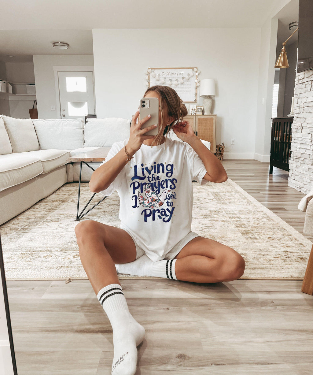 White unisex t-shirt with “Living the Prayers…Pray” front graphic