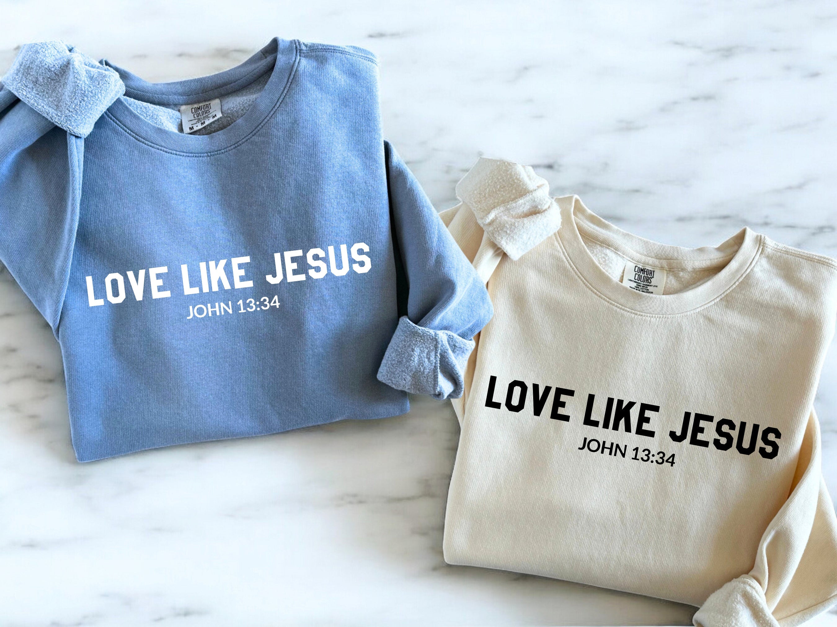 Pair of crewneck sweatshirts: blue and ivory, both with “LOVE LIKE JESUS” print