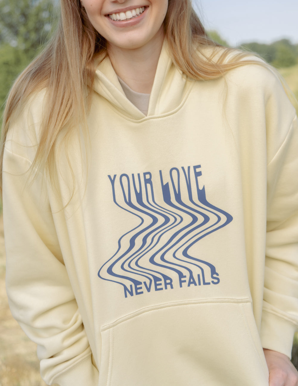 Cream unisex hoodie with blue 'Your Love' wave graphic and 'Never Fails' text