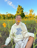 Cream unisex hoodie with blue wave graphic and 'Never Fails' text; hooded pullover