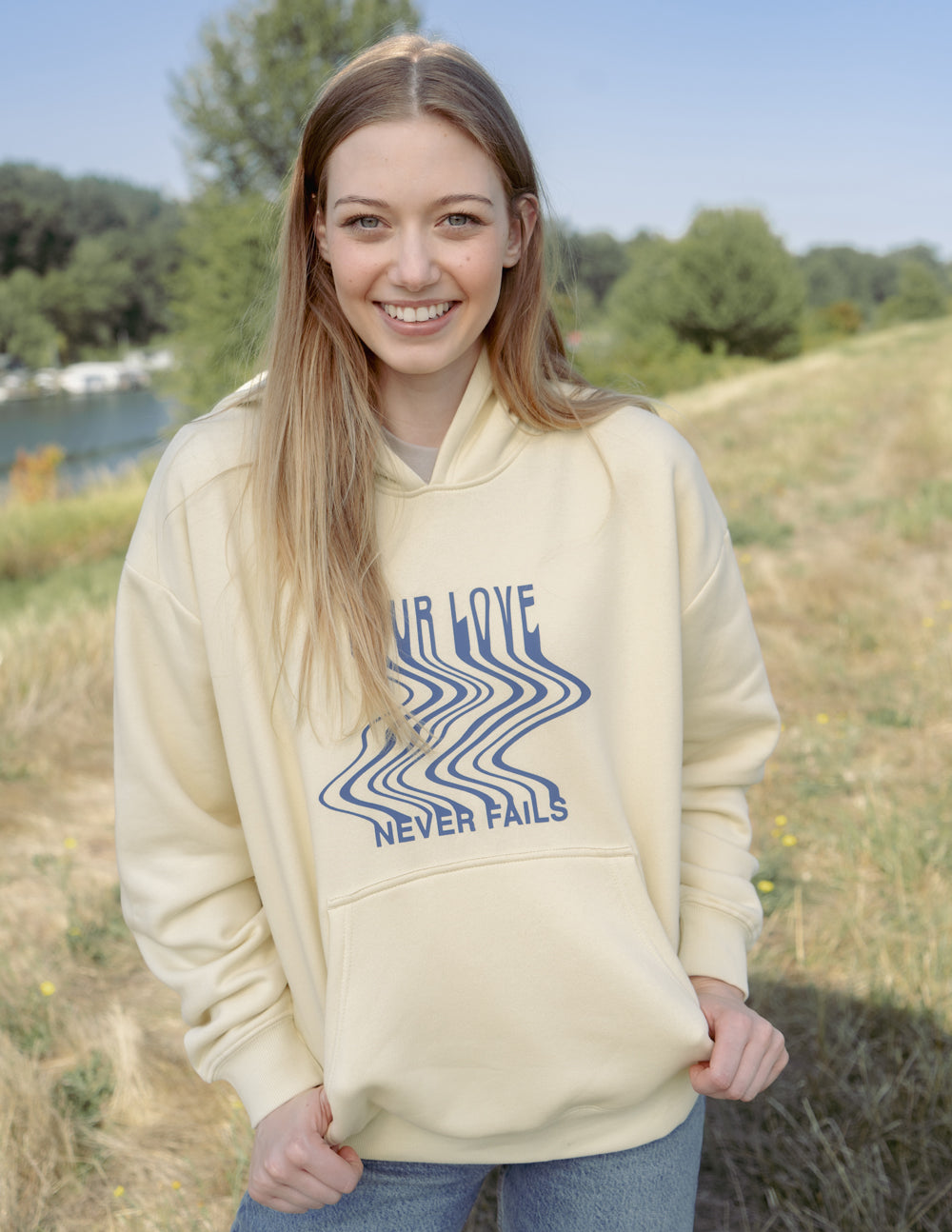 Cream unisex hoodie with blue 'Your Love Never Fails' graphic and front pocket