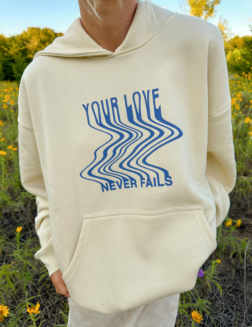 Cream unisex hoodie with blue wave 'Your Love' and 'Never Fails' graphic detail