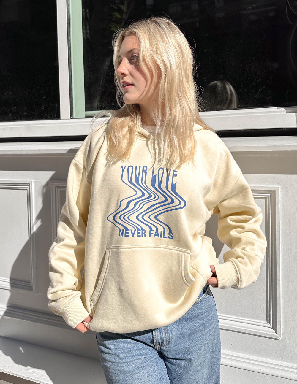 Cream unisex hoodie with blue chest graphic, hood with drawstring, and front pocket