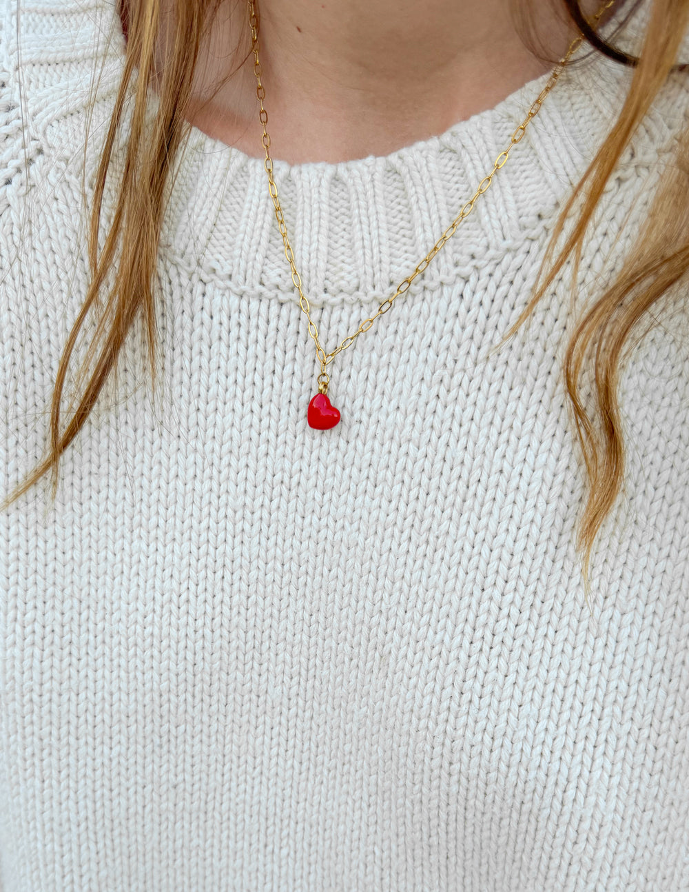 Gold paperclip chain necklace with red heart pendant on white knit sweater