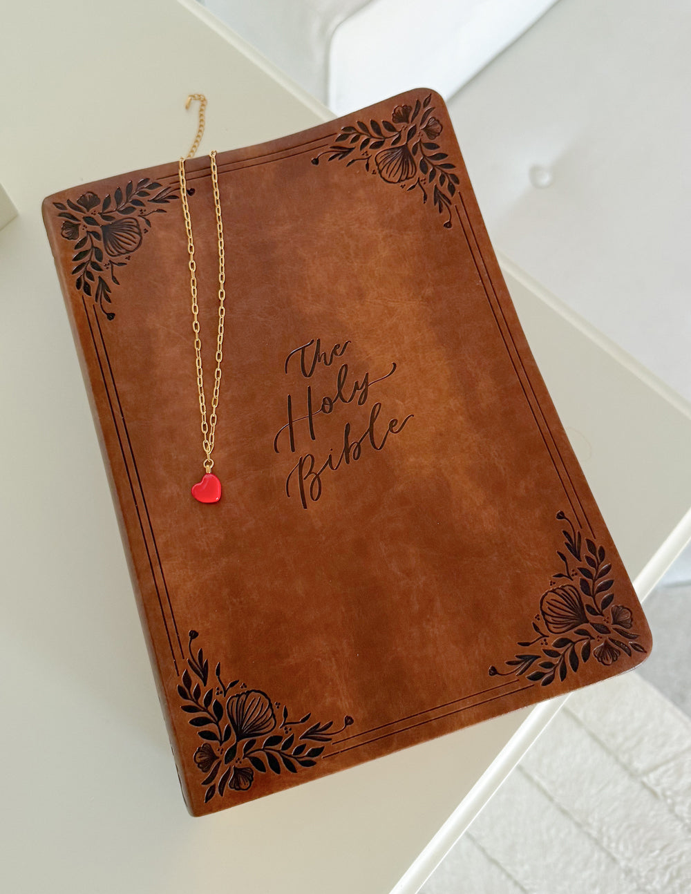 Gold paperclip chain necklace with red heart pendant on a display card